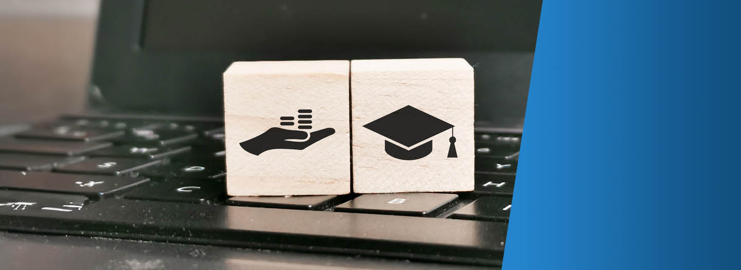 hand with money and graduation cap wooden tiles sitting on a laptop keyboard